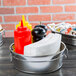An American Metalcraft stainless steel round metal tub filled with napkins and condiments.