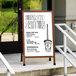 An Aarco cherry stained oak A-frame sidewalk sign with a white porcelain marker board.