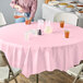A table with a pink Classic Pink OctyRound plastic tablecloth and glasses of yellow and orange liquid.