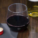 A clear plastic WNA Comet stemless wine goblet filled with red wine on a table next to a bottle of wine.