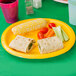 A Creative Converting School Bus Yellow oval paper platter with a burrito, tortillas, corn, tomatoes, and vegetables on it.