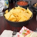 A large round charcoal polyethylene basket filled with chips on a table.