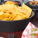 A large round charcoal polyethylene basket filled with tortilla chips on a table in a Mexican restaurant.