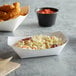 A white paper food tray with a bowl of coleslaw and chicken sticks.