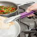 A person using Vollrath stainless steel tongs with a purple Kool Touch handle to serve salad.