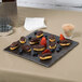 An American Metalcraft walnut melamine serving board with chocolate covered strawberries and chocolate covered eclairs on a table.