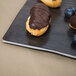 An American Metalcraft walnut melamine serving board with a chocolate covered pastry and blueberries on a table.
