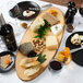 An oval melamine serving board with cheese, nuts, and wine on a table.