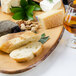 An oval melamine serving board with cheese, bread, and a glass of liquid on it.