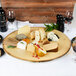 A round melamine serving board with cheese, fruit, and wine on a table.