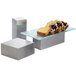 A piece of cake on a table with American Metalcraft stainless steel rectangular risers.
