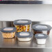 A group of Rubbermaid Premier food storage containers with black lids on a counter. One container has coffee beans and another has pasta.