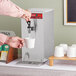 A person using an Avantco hot water dispenser to pour water into a white mug.