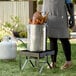 A woman using a Backyard Pro turkey fryer kit to cook chicken in a large metal pot.