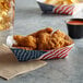 A paper food tray of fried chicken and fries with a USA flag on the table.