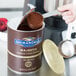 A person using a scoop to add Ghirardelli Dutch Cocoa Powder to a container.