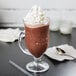A glass cup of Ghirardelli Chocolate Frappe mix with whipped cream and a spoon.