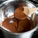 A wooden spoon stirring melted Ghirardelli dark chocolate in a metal bowl.