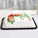 A 1/4 sheet cake with frosting and flowers under a clear dome lid.
