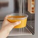 A hand using a Choice translucent plastic deli container to hold food in front of a microwave.