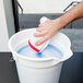 A hand holding a Unger Pill Glass Cleaner tablet over a bucket of water.
