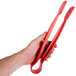 A hand holding a pair of red Thunder Group flat grip tongs.