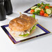 A Fineline white plastic plate with blue and gold bands holding a sandwich with a side salad.