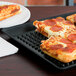 A close up of a pizza on a black HS Inc. Pizza Pleezer tray.