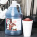 A jug of blue Carnival King root beer slushy syrup next to a white cup of slush