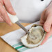 A person using a Mercer Culinary Boston style oyster knife to cut an oyster.