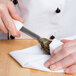 A person's hand using a Mercer Culinary New Haven style oyster knife with a white textured handle to shuck an oyster.
