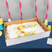 A white corrugated full sheet cake box with a cake decorated with pink and yellow flowers on it.