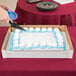 A person cutting a frosted cake with a black cake knife.