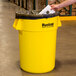 A person holding a yellow Continental Huskee trash can with a black plastic bag inside.