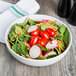 A white stoneware serving bowl filled with a salad of tomatoes, spinach, and radishes.