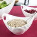 A white porcelain boat bowl filled with seeds and berries on a table with a spoon in it.