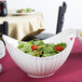 A white porcelain boat bowl filled with salad on a table.