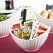 A white porcelain boat bowl with line texture filled with bread on a hotel buffet counter.