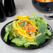A 10 Strawberry Street black stoneware salad plate with salad and vegetables and a bowl of soup on a table.