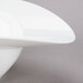 A close up of a 10 Strawberry Street Somba white porcelain rim bowl with a curved edge.
