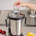 A hand pouring a black object into a Hamilton Beach stainless steel food blender.