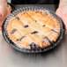A person holding a pie in a D&W Fine Pack black plastic container with clear low dome lid.
