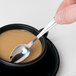 A hand holding a Libbey demitasse spoon in a cup of brown liquid.