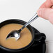 A hand holding a Libbey stainless steel demitasse spoon in a cup of coffee.