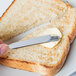 A person using a Libbey stainless steel butter spreader to spread butter on a piece of bread.