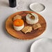 An American Metalcraft Faux Olive Wood round melamine charger with cheese and crackers on it.