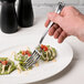 A hand holding a Libbey stainless steel dinner fork over food on a plate.