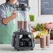 A woman in a commercial kitchen pours a smoothie into an AvaMix commercial blender on a counter.