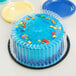 A blue cake with sprinkles on top sits on a yellow plate with a clear plastic container lid next to it.