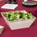 An American Metalcraft antique white melamine square bowl full of green and red salad on a table.